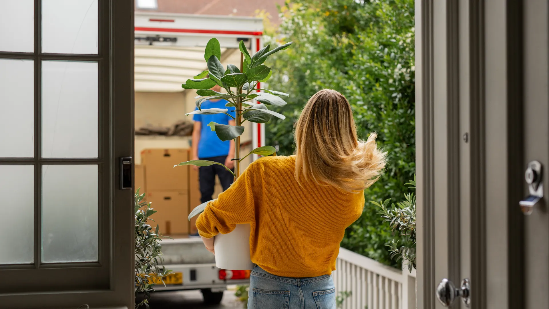 women in yellow carrying a plant to removal van